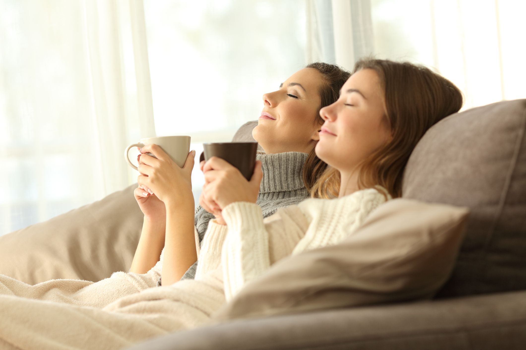Two ladies sitting on couch holding coffee. Two ladies sitting on couch holding coffee.